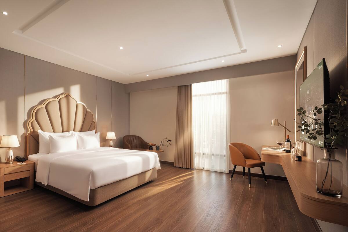 Habitación de hotel con una cama grande, un escritorio, una silla, una mesita de noche y un televisor instalado en la pared.