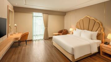 A hotel room with a large bed, a desk with a chair, a TV, and a window with curtains.