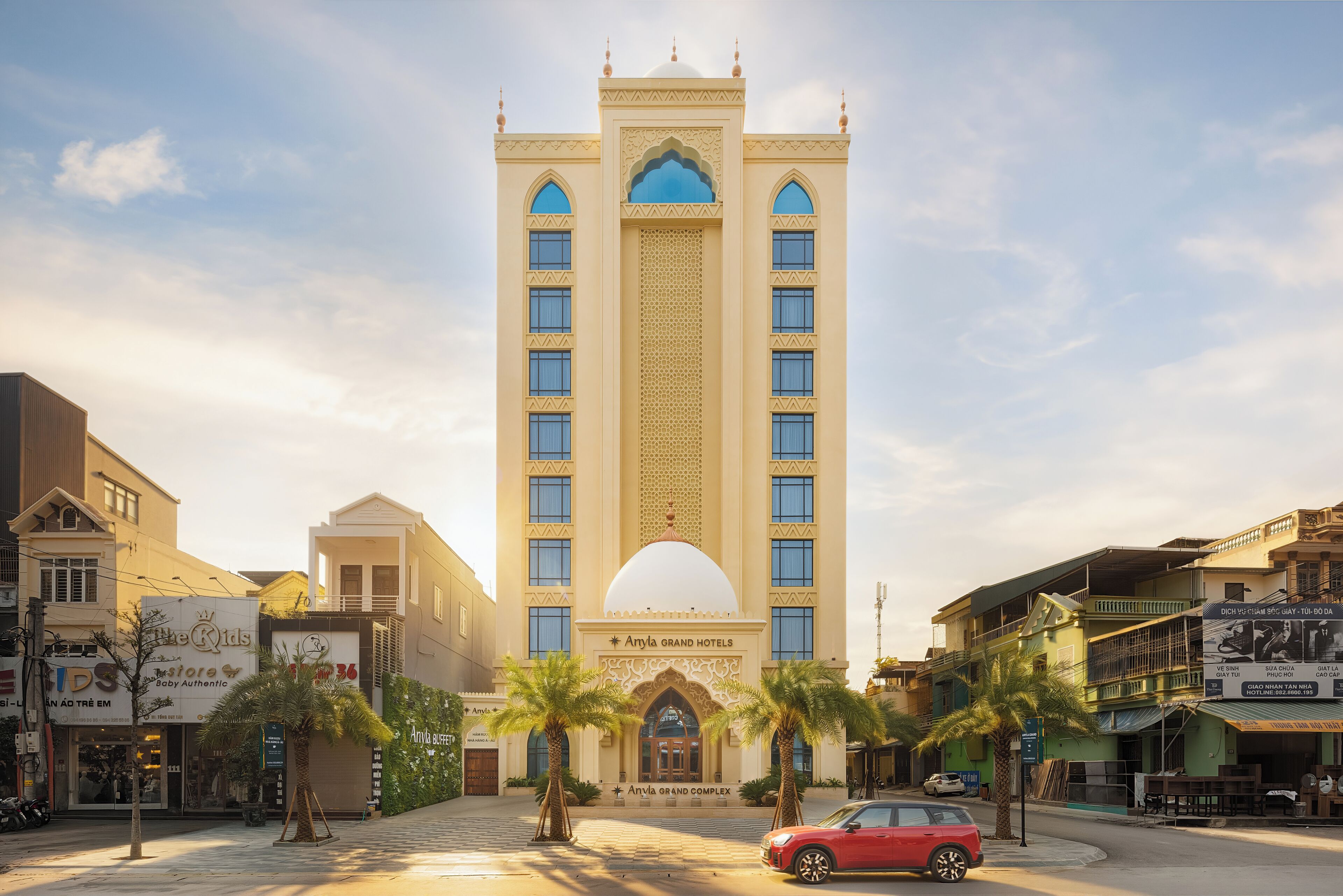 A hotel with a central dome and arched windows, surrounded by palm trees and other buildings.