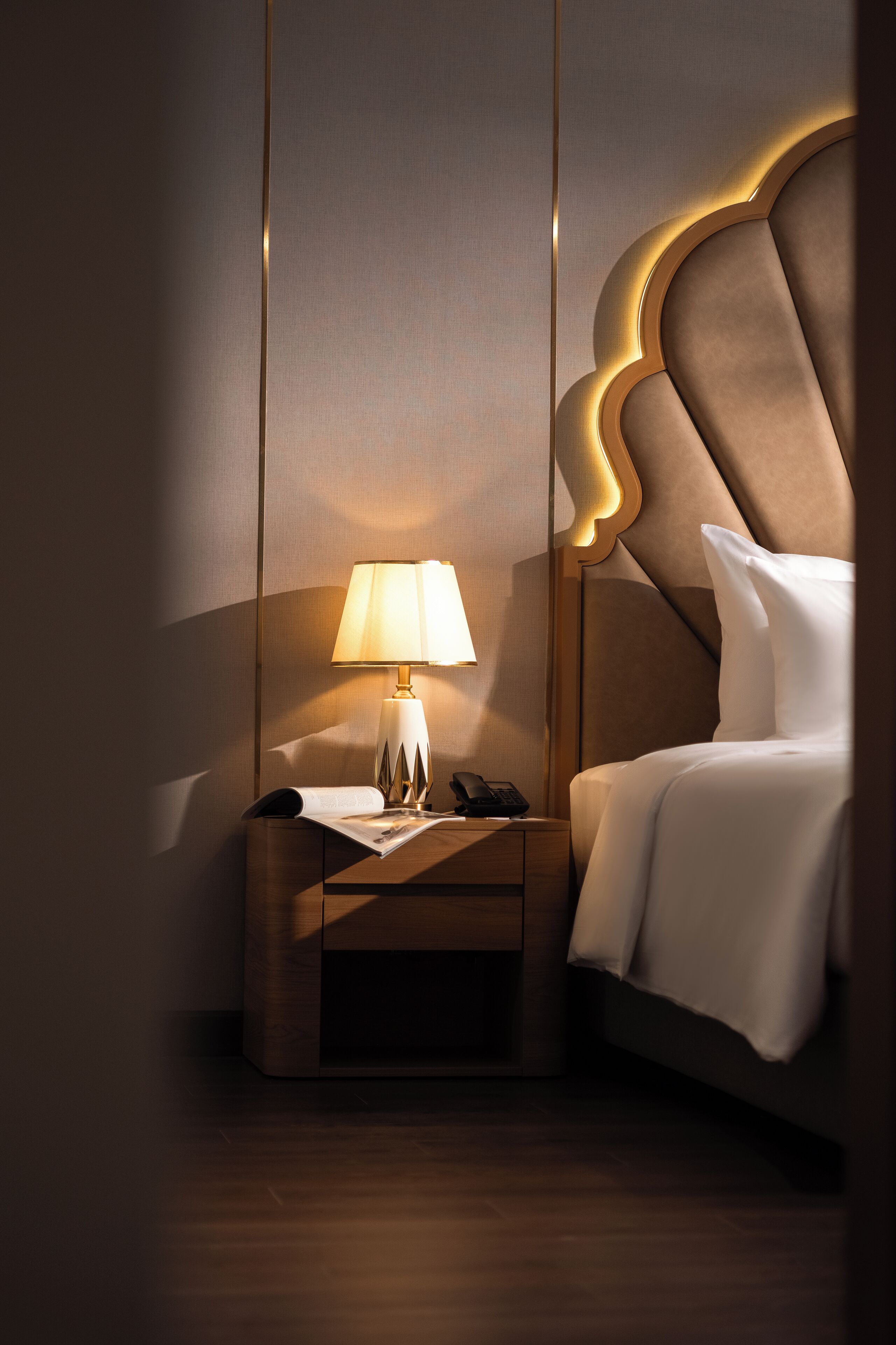 Una habitación de hotel con una cama grande, una mesita de noche con lámpara y un teléfono.