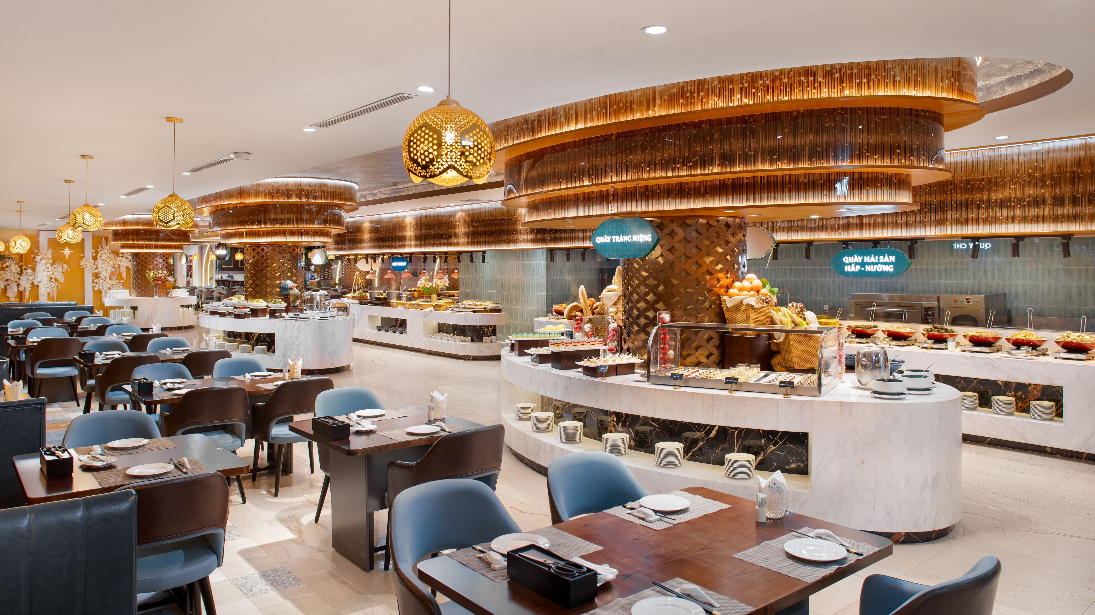 A modern restaurant with multiple dining areas, a buffet with various food options, and decorative lighting fixtures.