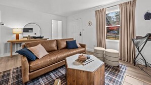 Ett modernt vardagsrum med en soffa i läder, ett soffbord och utsikt över naturen genom stora fönster.