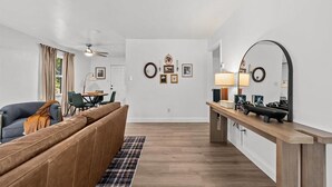 Ett modernt vardagsrum med en soffa, ett matbord och en köksdel med en spegel och en lampa.