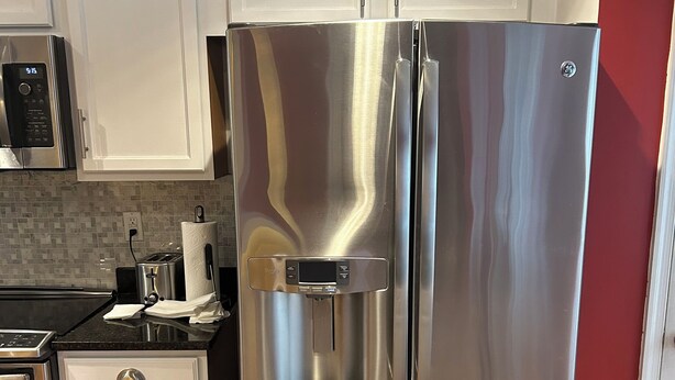 Ein Edelstahl-Kühlschrank mit Wasserspender, darüber eine Mikrowelle und ein Toaster auf der Arbeitsplatte.