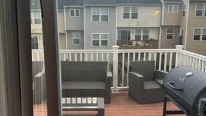 Eine Terrasse mit Gartenmöbeln und Grill, mit Blick auf eine Reihe von Reihenhäusern.