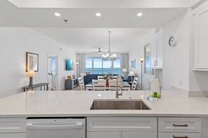 A modern kitchen with a central island, a dining area with a view, and a living room with a sofa and a TV. - Beach Front Unit-Tops'l Resort-Pickleball Courts-Covered Parking-Tides 804 (Miramar Beach)