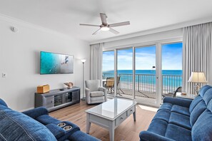 A modern living room with a large window overlooking the ocean, a ceiling fan, and a flat-screen TV mounted on the wall. - Beach Front Unit-Tops'l Resort-Pickleball Courts-Covered Parking-Tides 804 (Miramar Beach)