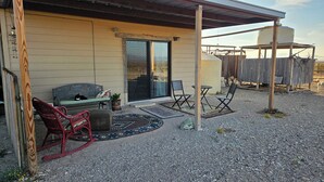 A covered patio with a bench, two chairs, and a small table. - THE FAR SIDE OF THE MOON
Off Grid 1-bedroom  "Cowboy Camp" in the desert (Terlingua)