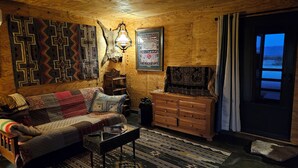 A cozy living room with a wooden interior, a sofa, a coffee table, a TV, and a large window with curtains. - THE FAR SIDE OF THE MOON
Off Grid 1-bedroom  "Cowboy Camp" in the desert (Terlingua)