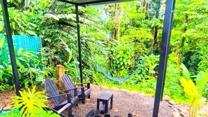 A covered outdoor seating area with chairs and a table, surrounded by a garden with various plants and a hammock. - Monstera Forest Lodge #2 (Provincia de Alajuela)