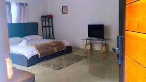 A bedroom with a bed, a TV on a stand, a small table, and a window with curtains. - Monstera Forest Lodge #2 (Provincia de Alajuela)