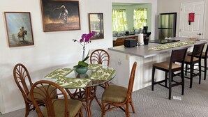 Ein Essbereich mit Tisch, Stühlen und einem Blumenstrauß. An der Wand befinden sich gerahmte Bilder und durch eine offene Tür ist eine Küche zu sehen.