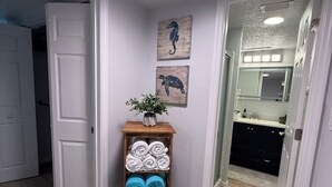 Un pasillo con un estante de madera que contiene toallas, una puerta que da a un baño y una pared decorada con dos cuadros de caballitos de mar.