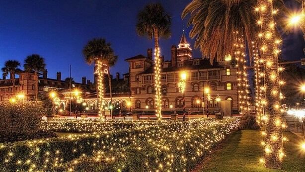 Un edificio histórico con un jardín formal, iluminado por luces colgantes y palmeras.