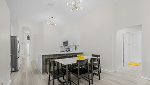 Een moderne keuken met witte kastjes, een centraal eiland en een eethoek met een tafel en stoelen.