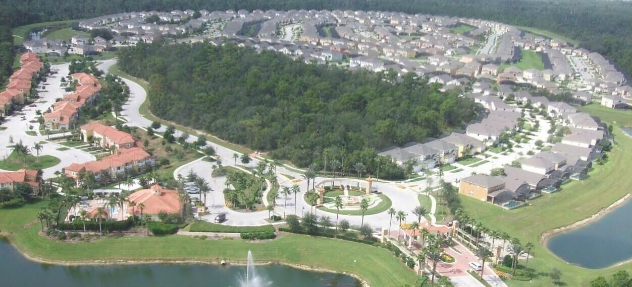Une vue aérienne d’un quartier résidentiel avec des maisons, un parc central et une étendue d’eau.