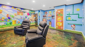 Een kamer met een muurschildering in Mario-thema, twee zwarte leren stoelen en een Nintendo 64 spelconsole.