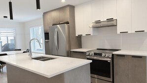 Une cuisine moderne dotée d’un îlot central, d’appareils électroménagers en acier inoxydable et de meubles de rangement blancs.