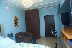 A bedroom with a bed, a wardrobe, a television, and a fan.