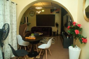 Un área de comedor con una mesa, sillas, un sofá, un televisor y una planta decorativa.