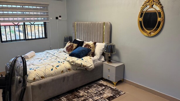 Une chambre à coucher avec un lit, une table de chevet, une lampe et un grand miroir au mur.