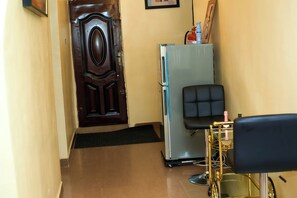 A hallway with a door, a refrigerator, a chair, and a cart with a bottle.