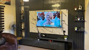 Un salon moderne doté d’un grand téléviseur à écran plat fixé sur un mur de marbre, d’un meuble de rangement en bois foncé et d’un confortable canapé marron.
