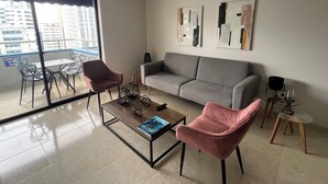 Un salon moderne avec un canapé gris, deux fauteuils roses, une table basse et une œuvre d’art abstraite accrochée au mur.