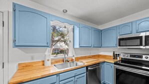 Eine Küche mit blauen Schränken, einer Holzarbeitsplatte, einer Edelstahlspüle, einem Geschirrspüler, einer Mikrowelle und einem Backofen.