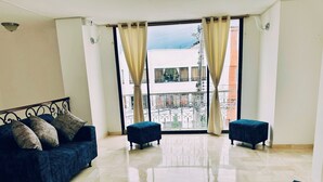 Un'ampia stanza con un'ampia finestra, un divano, due poggiapiedi e un letto con struttura in metallo.