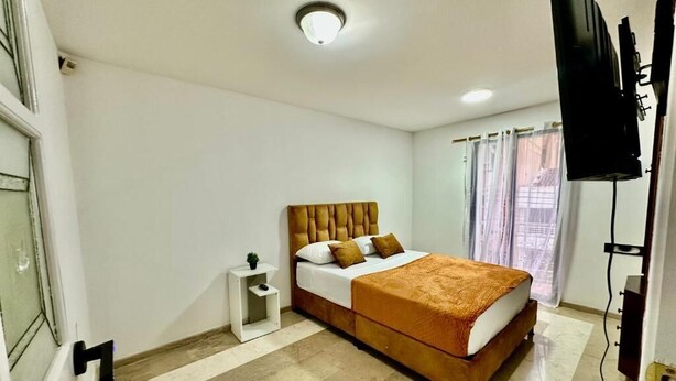 Una camera da letto con un letto, un comodino, una televisione e una finestra con tende.