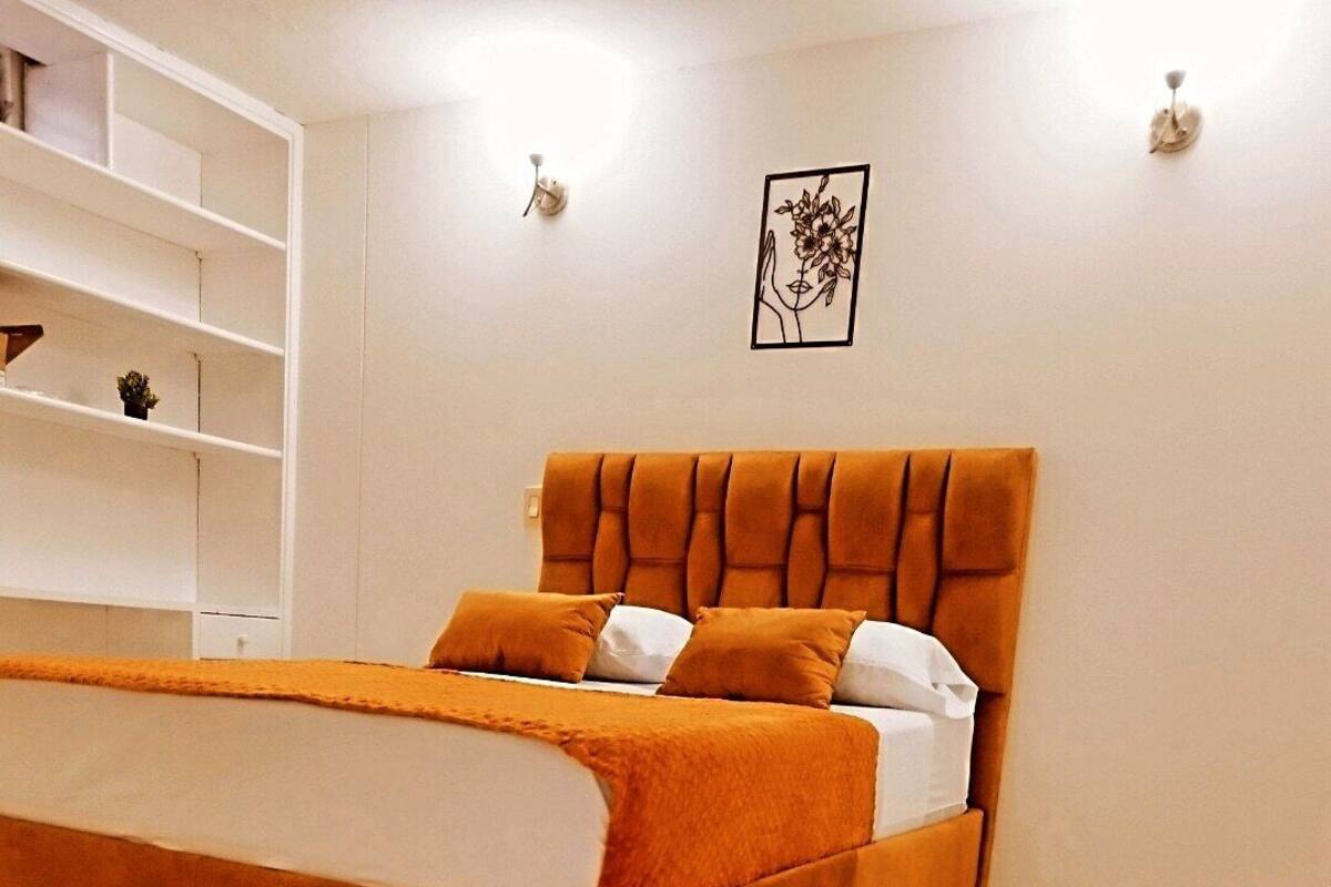 Un dormitorio con cama, estantería blanca y un cuadro colgado en la pared.