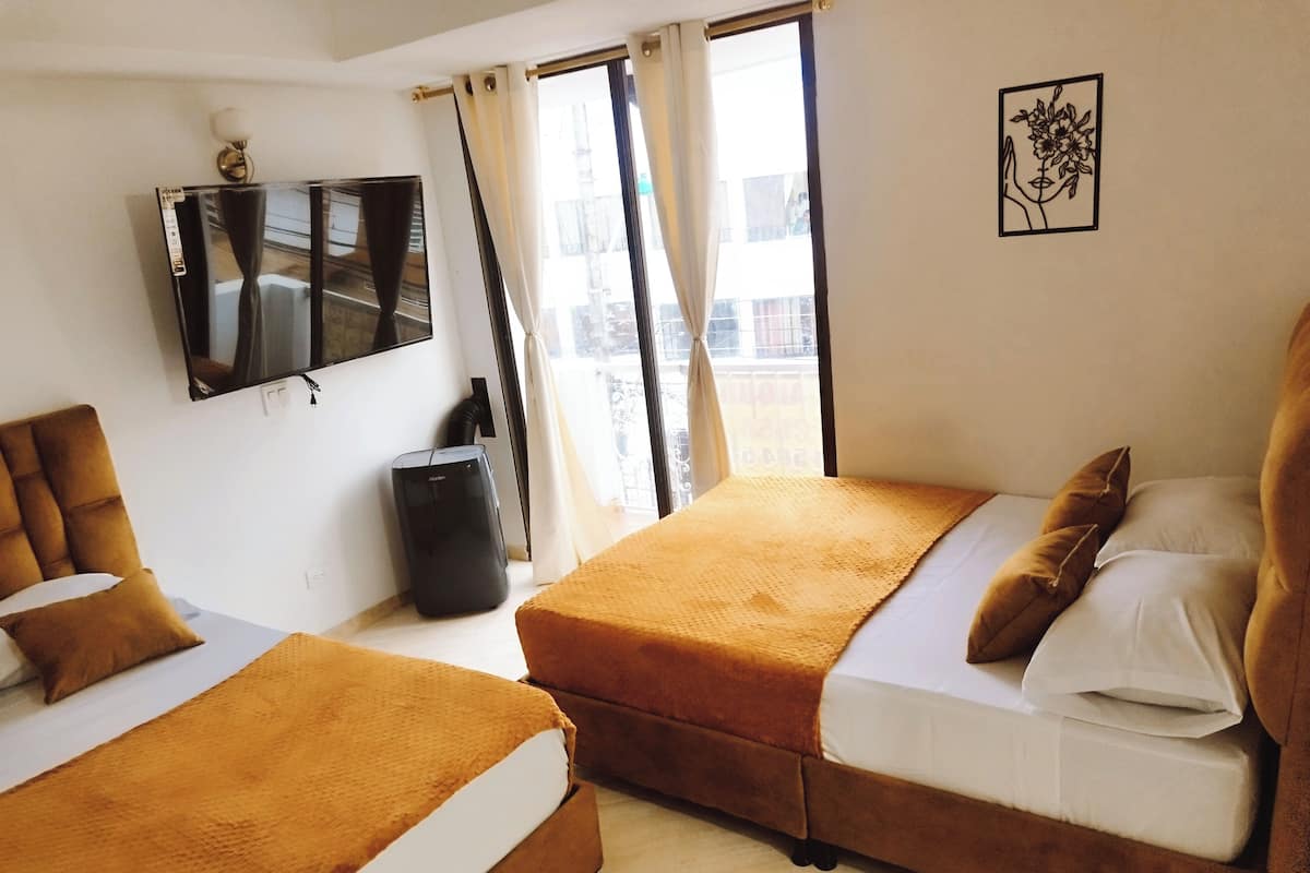 Habitación de hotel con dos camas, televisión, cubo de basura y ventana con cortinas.
