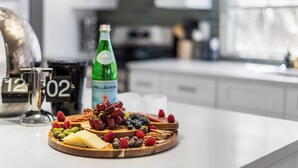 Een aanrecht met een fruitschaal, kaas, een fles bruisend water en een koffiemachine.