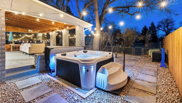 Een moderne buitenjacuzzi met houten terras, stenen trappen en lichtslingers.