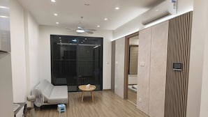 A modern hotel room with a ceiling fan, air conditioning unit, a sofa, a small table, and a sliding door leading to a balcony.