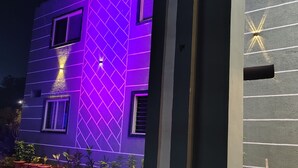 Een gebouw met een paars geometrisch patroon op de gevel, meerdere ramen en potplanten langs de grond.