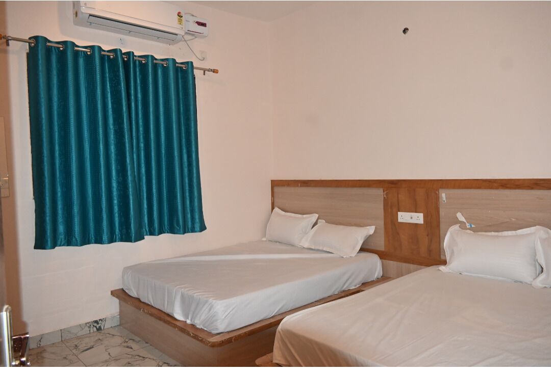 Une chambre d’hôtel avec deux lits simples, une tête de lit en bois, un rideau de couleur turquoise et un appareil de climatisation fixé au mur.