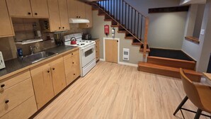A compact kitchen with wooden cabinets, a stove, and a sink. There is a staircase leading to a lower level. - Amazingly convenient central location in Rossland with everything you need! (Rossland)