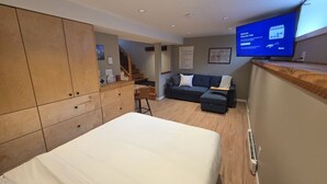A modern hotel room with a bed, a desk, a sofa, and a TV displaying a welcome message. - Amazingly convenient central location in Rossland with everything you need! (Rossland)