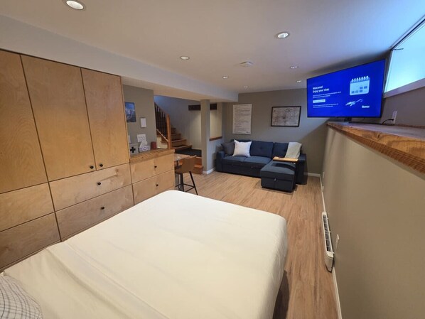 A modern hotel room with a bed, a desk, a sofa, and a TV displaying a welcome message.