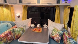 A cozy interior with a table and two blue cushioned benches, yellow curtains, and a decorative sign above.