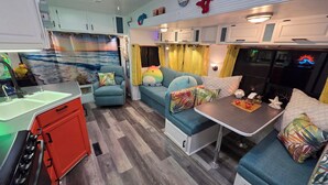 A compact RV interior with a kitchenette, a dining area, and a seating space with colorful cushions.
