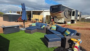 A recreational vehicle (RV) with a large awning, a lounge area with wicker furniture and cushions, and a well-maintained lawn.