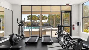 Una palestra con tapis roulant, macchinari ellittici e attrezzature per pesi. Dispone di ampie finestre che offrono vista su palme e una piscina.