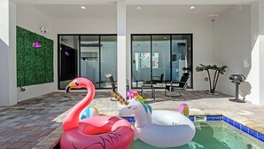 Una piscina con giochi gonfiabili, ingresso con porta in vetro e parete verde.