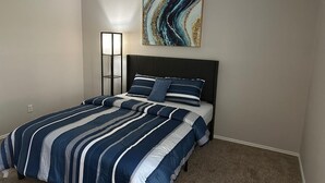 Une chambre à coucher comprenant un lit, une table de chevet, une lampe sur pied et un tableau abstrait accroché au mur.