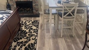 Un salon avec une cheminée, une table à manger avec des chaises, un lit et une grande fenêtre avec des stores.
