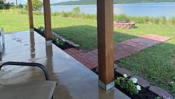 Une terrasse couverte offrant une vue sur un lac et des collines lointaines.