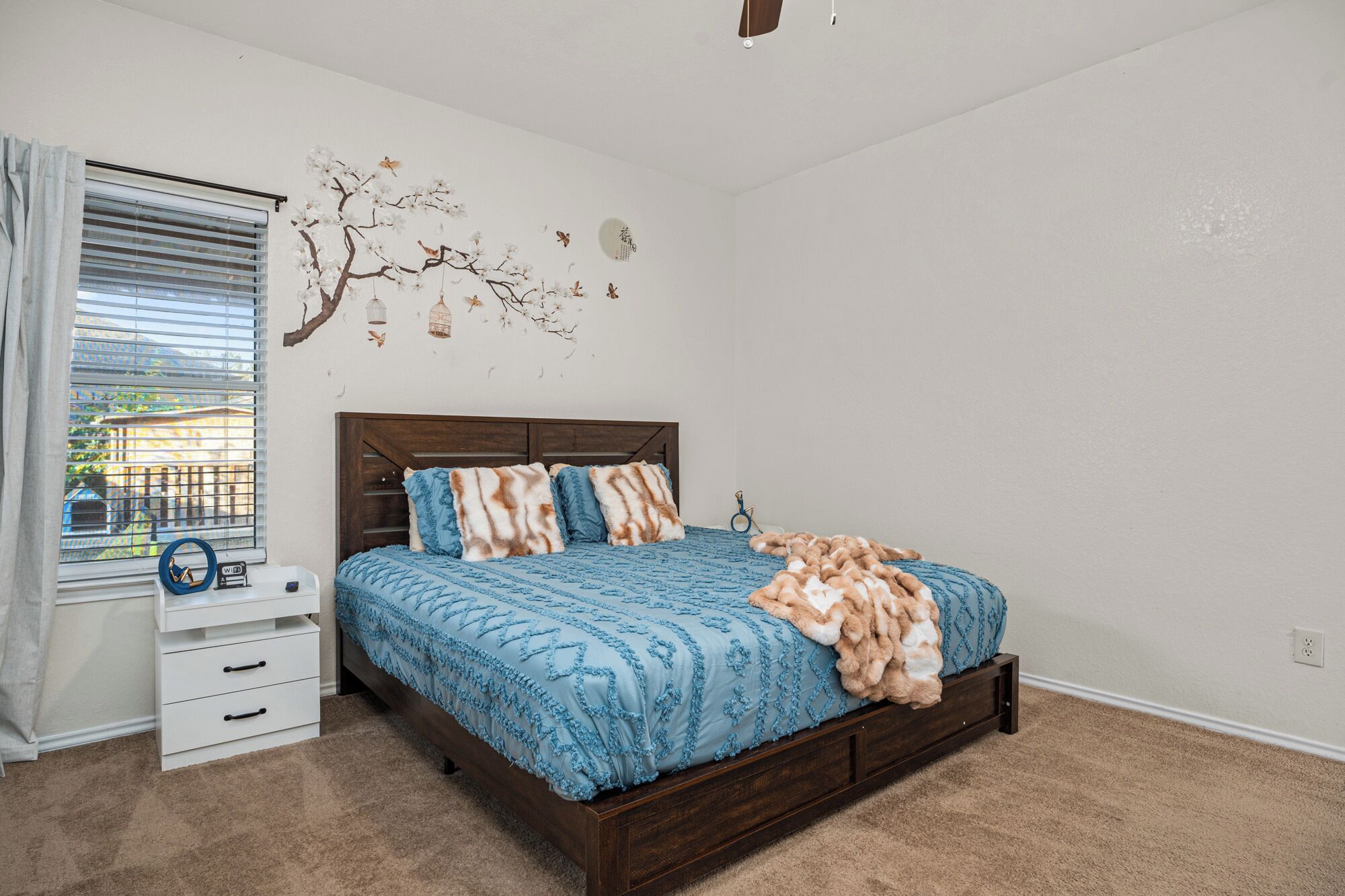 A bedroom with a bed, a nightstand, and a window with blinds.